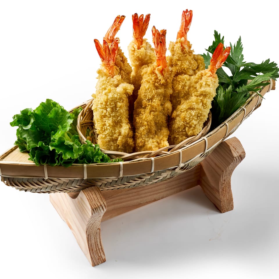 Basket of golden-brown breaded shrimp garnished with lettuce and parsley on a wooden stand.