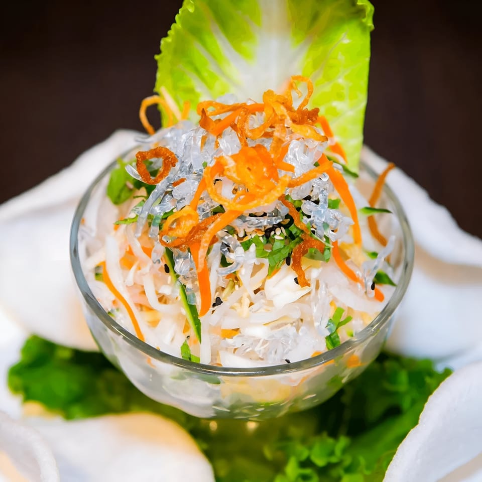 Vietnamese vegetarian salad with clear noodles, shredded carrots, and greens in a glass bowl.