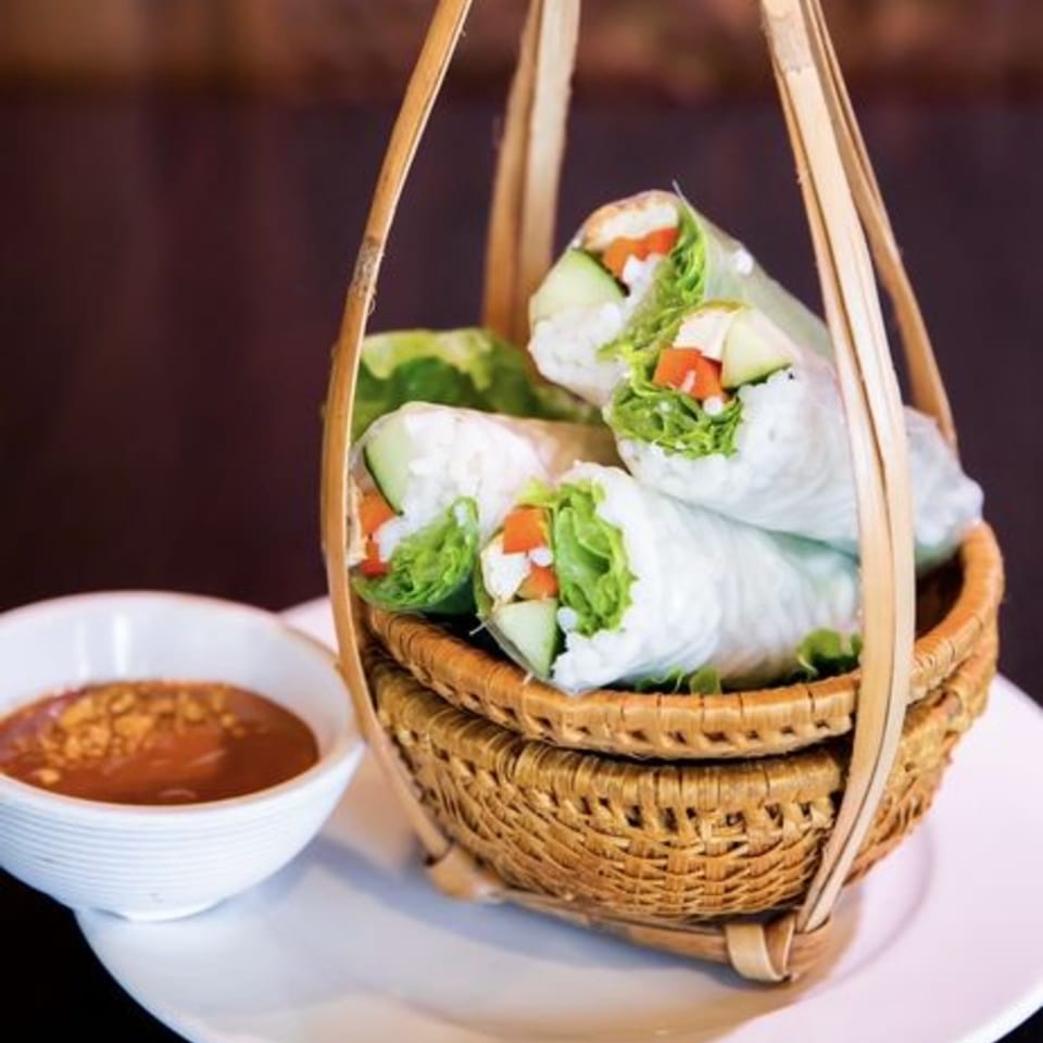 Vietnamese spring rolls with fresh vegetables and tofu in a woven basket, with peanut dipping sauce.