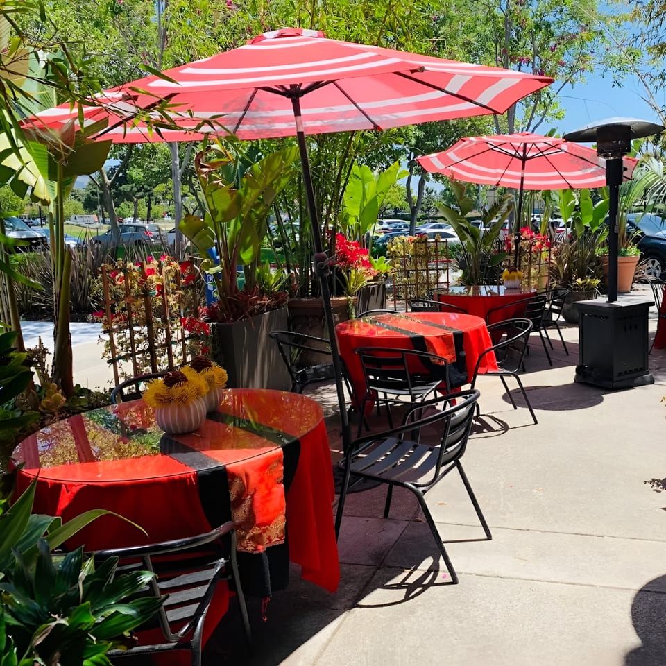 Outdoor patio dining at Golden Bamboo with red umbrellas, tables, and lush green plants.
