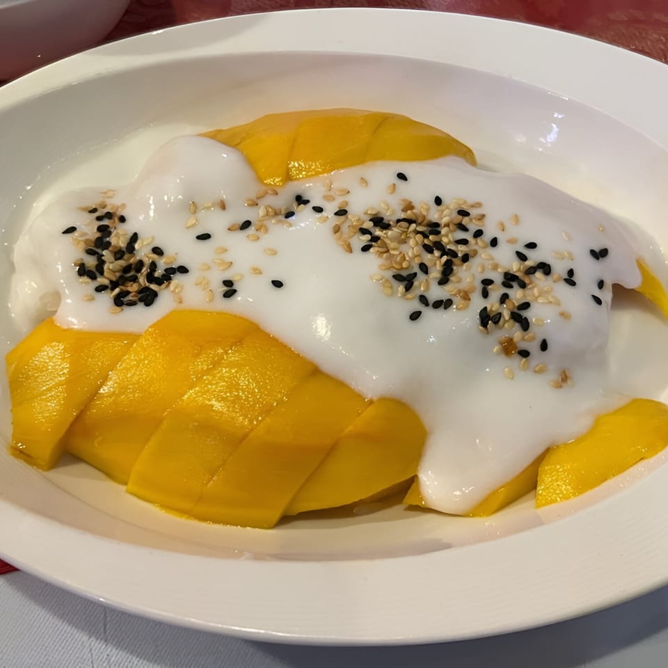 Sliced mangoes topped with white coconut cream and sesame seeds in a white bowl.