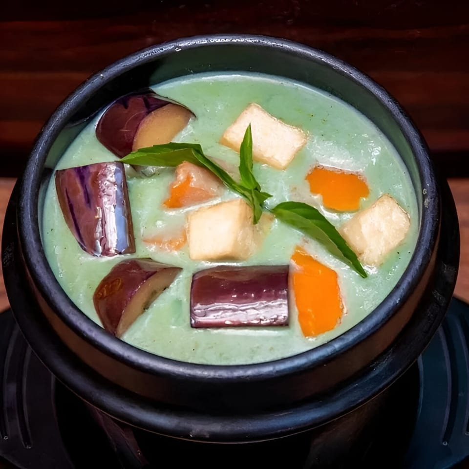 Green curry with eggplant, tofu, and orange vegetables in a black bowl.