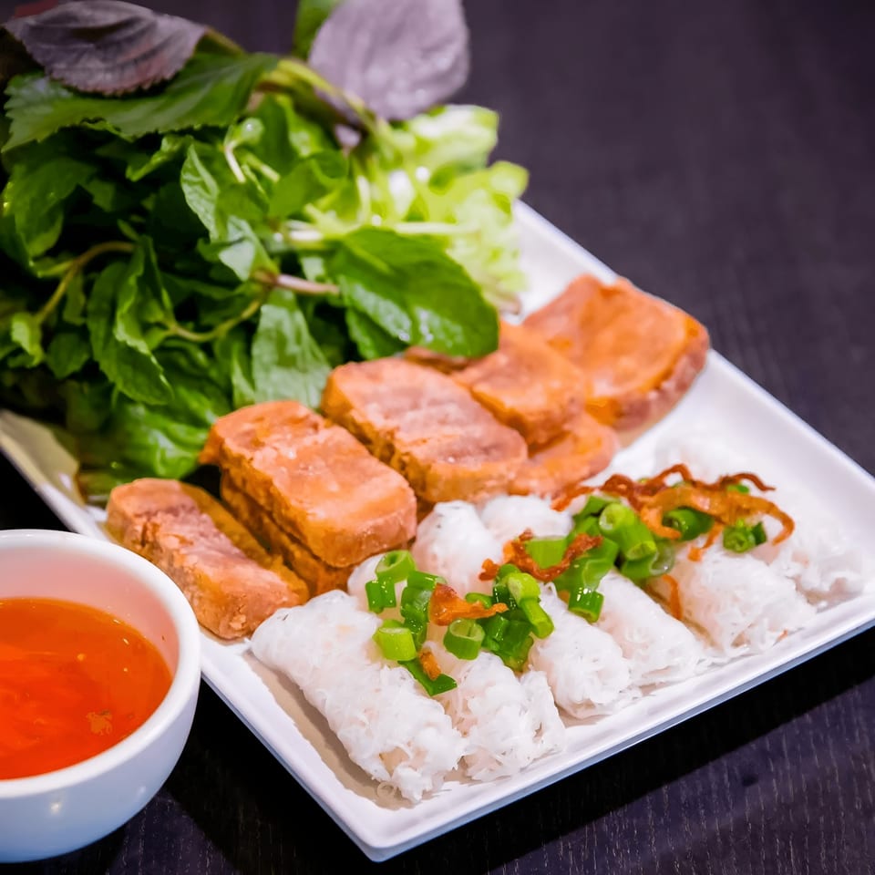 Vietnamese vegetarian dish with fried tofu, fresh herbs, rice noodle rolls, and a dipping sauce.