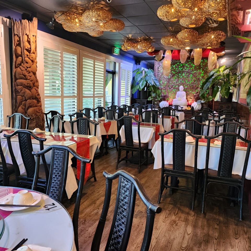 Empty dining room at Golden Bamboo Vegetarian Restaurant with black chairs, white tablecloths, and red runners.