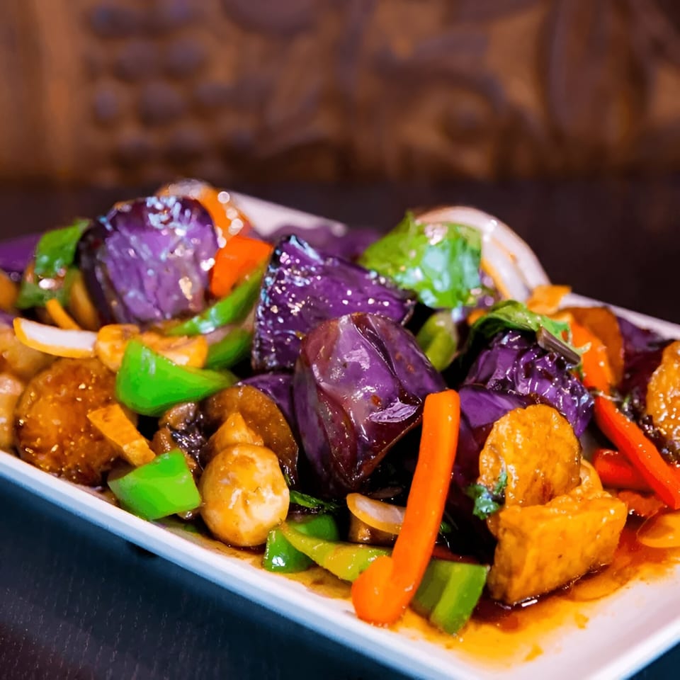 A vibrant Vietnamese stir-fry with purple eggplant, green and orange bell peppers, and tofu in sauce.